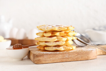 Delicious Belgian waffles with powdered sugar and honey on board on table against white background