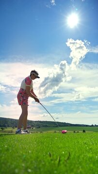 Active senior woman playing golf on a scenic course with rolling hills, enjoying outdoor exercise and vibrant retirement on a sunny summer day.