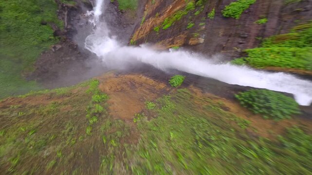 FPV drone diving over Kapas Biru waterfall and flowing jungle river in East Java, Indonesia. Dynamic aerial flight through lush tropical rainforest landscape in Southeast Asia.