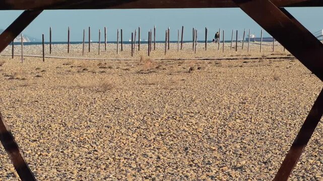 Authentic Empty Wooden Archway On Pebble Beach With Distant Man Walking Dog Golden Hour Establishing Shot
