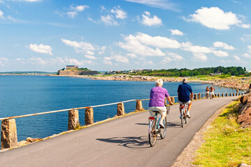 Fototapeta premium Cyclists on coastal path near a historic fortress in The swedish town Varberg