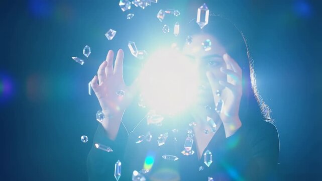 A woman positions her hands among floating crystals in a dark environment, revealing reflections and highlights. creative, beauty, or technology projects