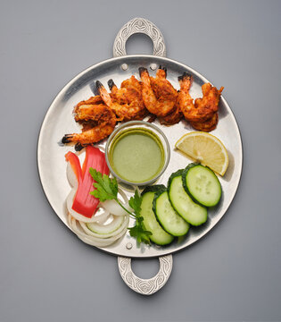 Shrimp and vegetables served on a metal plate with sauce and garnishes in a simple setting