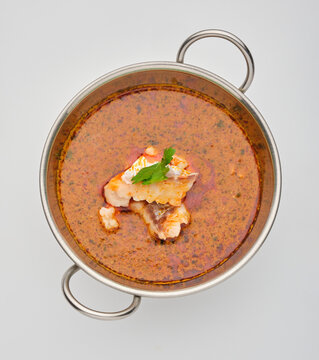 Seafood stew is served in a stainless steel pot with herbs on top