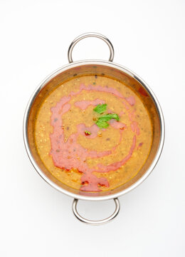 Warm lentil soup served in a metal pot with a swirl of sauce on top at a kitchen table in daytime