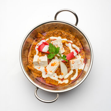 Dish of paneer curry served with fresh herbs on a white background in a metal serving bowl