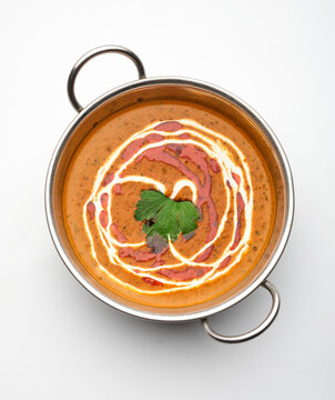 Delicious bowl of creamy soup with swirls of sauce and herbs served in a stainless steel pot on a white background
