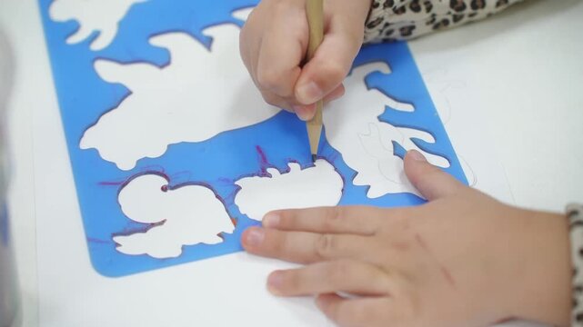 A girl on a stencil circles animals with a pencil. Kindergarten classes. Close-up. High quality video