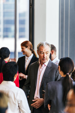 Professionals in suits network and converse at a corporate event near large windows in a modern office building.