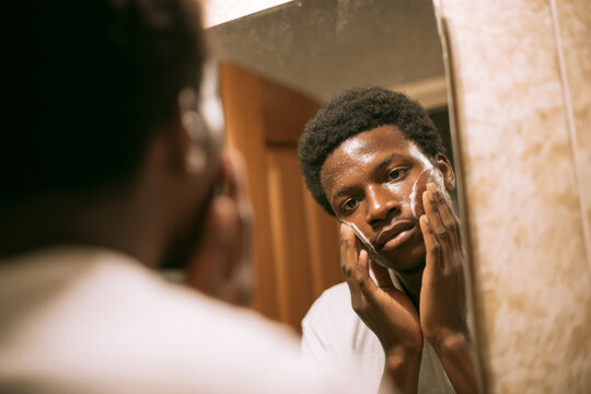 African college student washing face late evening, cozy apartment bathroom, warm indoor lighting, mirror reflection composition