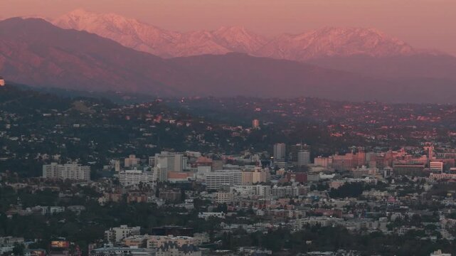 Aerial telephoto dolly shot of Hollywood with snow-covered mountains in the background during magic hour in Los Angeles, California. 4K