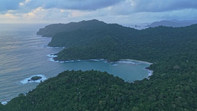 Dramatic aerial perspective of the rugged coastline of red island in java, showing a secluded bay with turquoise water and dense green jungle
