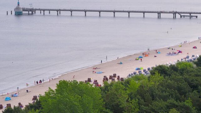An aerial view shows the Binz beach with a lot of sunbathers on R&uuml;gen stretching into the Baltic Sea, lined with a busy sandy beach and classic resort architecture.