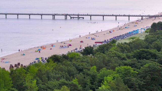 An aerial view shows the Binz beach with a lot of sunbathers on R&uuml;gen stretching into the Baltic Sea, lined with a busy sandy beach and classic resort architecture.