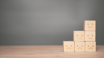 Mental health awareness concept with wooden cube blocks displaying happy neutral and sad faces arranged in pyramid representing emotional balance mood evaluation wellbeing and psychological awareness.