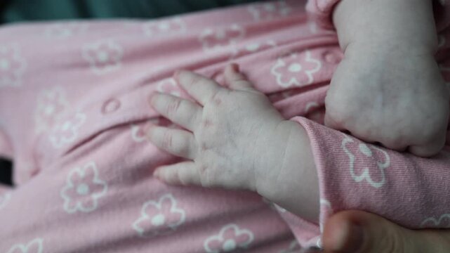 Extreme close-up of a tiny newborn baby's hand resting on a pink floral fabric. The small fingers and skin texture are visible