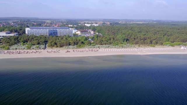 An aerial view shows the Binz beach on R&uuml;gen stretching into the Baltic Sea, lined with a busy sandy beach and classic resort architecture.