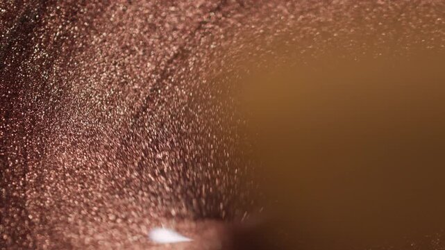 Dynamic close-up of copper paint with sandy texture being swirled by a wooden stick creating deep ridges and sparkling waves on black background