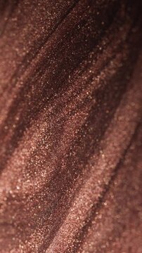 Abstract vertical macro shot of dark copper paint flowing diagonally with thick sandy texture and shimmering glitter particles on surface