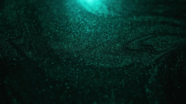 Detailed rotating close-up of dark golden paint under cyan light with specialized sandy texture and radiant glitter particles sweeping and flowing on abstract background