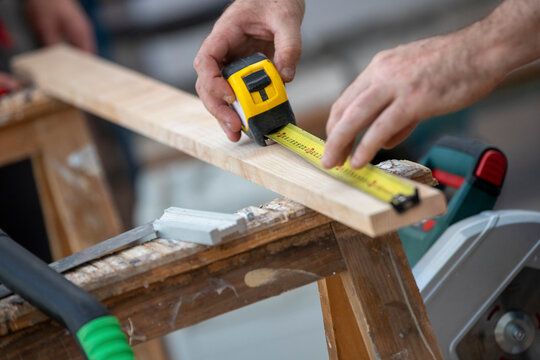 Menuisier effectuant une mesure avec un m&egrave;tre sur une planche de bois sur des tr&eacute;teau &agrave; l'int&eacute;rieur d'un b&acirc;timent. Menuisier exp&eacute;riment&eacute;, habile et comp&eacute;tent, prenant des mesures pour cr&eacute;er un meuble
