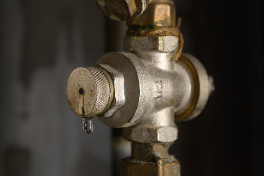 Leaking water pressure regulator on metal pipe in dark utility room signals home plumbing fault and need for urgent service.