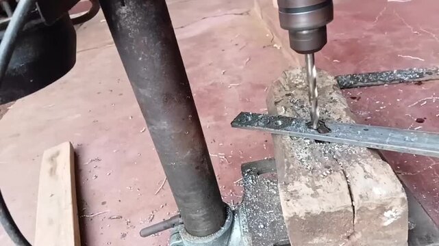 Slow motion close up of a bench drill press cutting a hole in a metal bar with smoking cutting oil and flying metal chips.