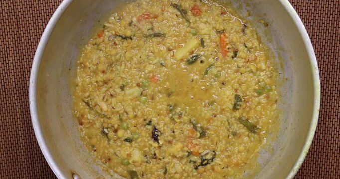 south Asian rice lentils khichuri khichdi soft runny porridge with diced vegetable boiling sizzling in a pot over flame top flatly view 