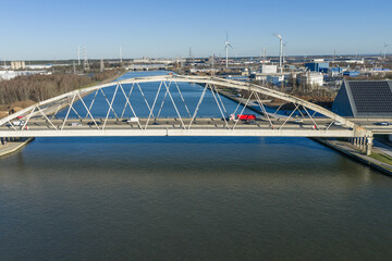 Fototapeta premium Aerial, drone view of bridge in Diepenbeek on the Albert Canal. Some traffic on the bridge. Large infrastructure, freight transport by water. Industry and wind turbines in the background. Alternative