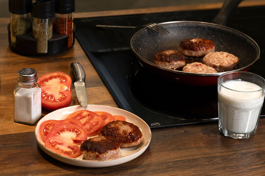 Traditional Balkan grilled minced meat dishes, kebapcheta and meatballs, being cooked in a frying pan in a home kitchen