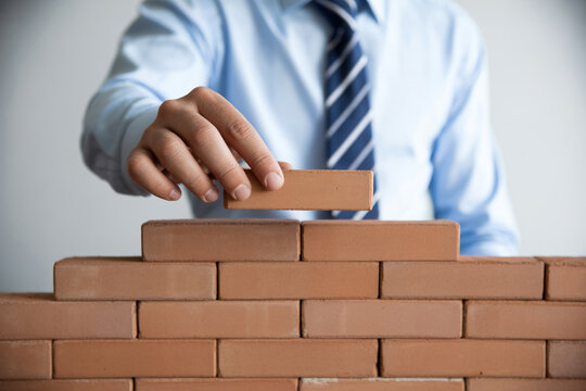 A businessman carefully places a final brick onto a partially constructed wall.