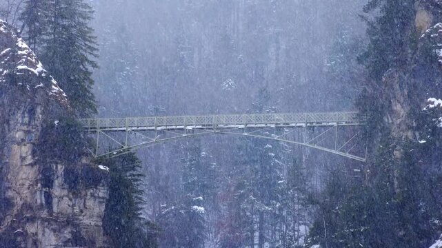 Cinematic winter video of the famous Marienbr&uuml;cke (Mary's Bridge) spanning across a deep gorge near Neuschwanstein Castle during a heavy snowstorm, Bavaria, Germany.