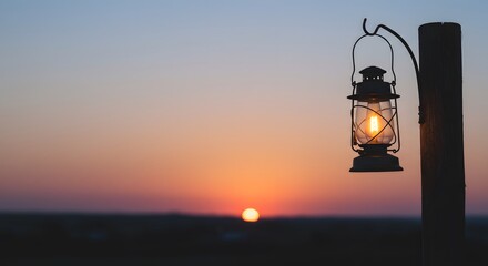Obraz premium Vintage Lantern Hanging on Wooden Post at Sunset with Warm Glow in Calm Outdoor Scene