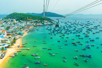 Cable car cabin gliding above turquoise sea with fishing boats and coastal village in Phu Quoc island, Vietnam Aerial view. Island transportation and tourism infrastructure © samael334