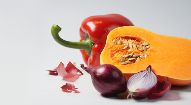 Macro shot of a halved butternut squash with visible seeds, red bell pepper, and red onions on gray. A fresh seasonal harvest background with copy space for text. Soft blur on organic farm vegetables.