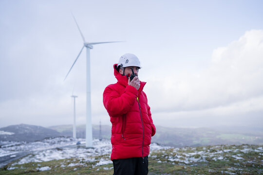 Worker in red jacket using radio for communication near wind turbine