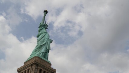 Obraz premium Statue of Liberty on Liberty Island, New York, United States. Blue cooper monument, symbol of democracy and patriotism near Manhattan, NYC USA. Clouds on sky. American independence. Torch and crown.