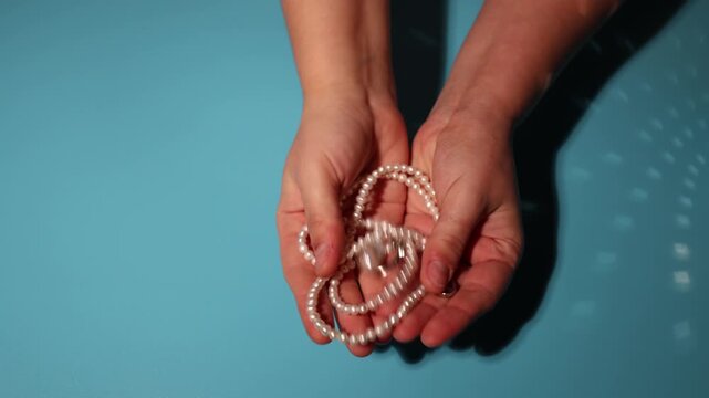 Hands holding a tangled strand of pearls against a bright blue background