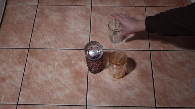 Hand arranging decorative glass candle holders on a tiled surface
