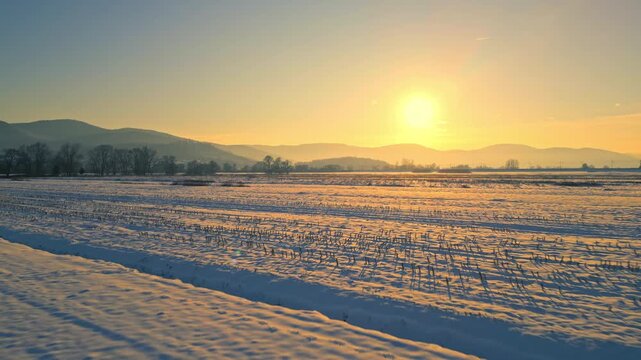 Serenely beautiful winter sunset over snow-covered fields and distant mountains, ideal for winter travel and nature photography.