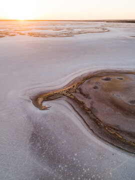 Aerial view of the stark white salt flats contrasting with the ochre earth tones under a golden sunrise sky, Lake Campion Nature Reserve, Western Australia, Australia.