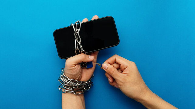 Hands chained to a smartphone being unlocked with a key. A conceptual image representing digital addiction, freedom from technology, phone dependency, and the journey of a digital detox process.