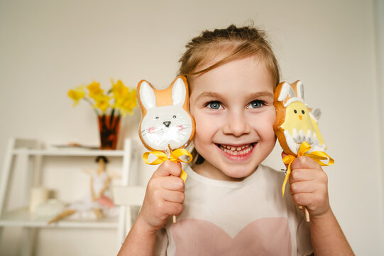 Smiling child holding bunny and chick Easter cookies at home
