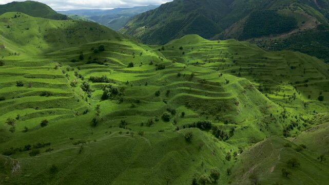 Drone aerial view of terraced fields near Chokh village in Dagestan, Russia in warm morning sunlight creating beautiful light and shadow across the Caucasus mountain landscape.