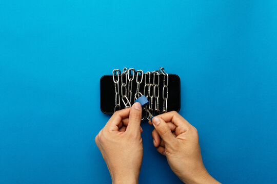 A person using a key to unlock a smartphone bound in heavy metal chains. Conceptual image for overcoming digital addiction, achieving freedom from technology, and the success of a digital detox.