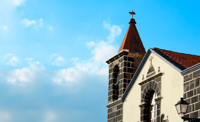 A close-up of a rustic church bell tower and a section of a building with stone details against a beautiful blue sky. The image highlights traditional European architecture and religious heritage.