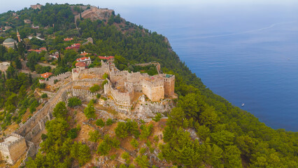 Fototapeta premium Alanya, Turkey. Ehmedek Castle emerging from green forest on mountainside, aerial drone view in summer morning.. Aerial View