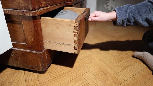 Hand opening a vintage wooden dresser drawer with clothes inside