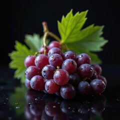 Naklejka premium Red grapes with water drops sit on dark reflective surface. Green leaves are visible behind fruit bunch. Evening light creates moody atmosphere.