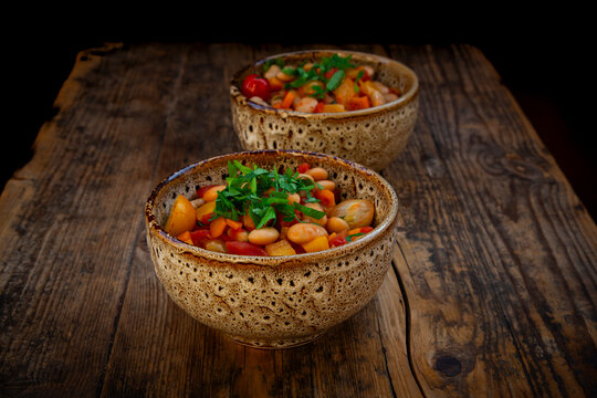 Rustic bean stew with broad beans and herbs in bowls on wooden table